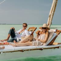 Flitterwochen Ziele können entspannend, aber auch abenteuerreich sein. Mann und Frau mit Sonnenbrillen und sommerlicher Kleidung liegen auf einer Liege über dem Meer.