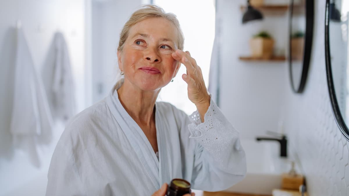 Ältere Frau trägt Augencreme mit Lichtschutzfaktor auf.