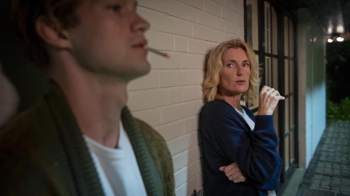 Maria Furtwängler raucht mit einem Mann und lehnt an der Wand.