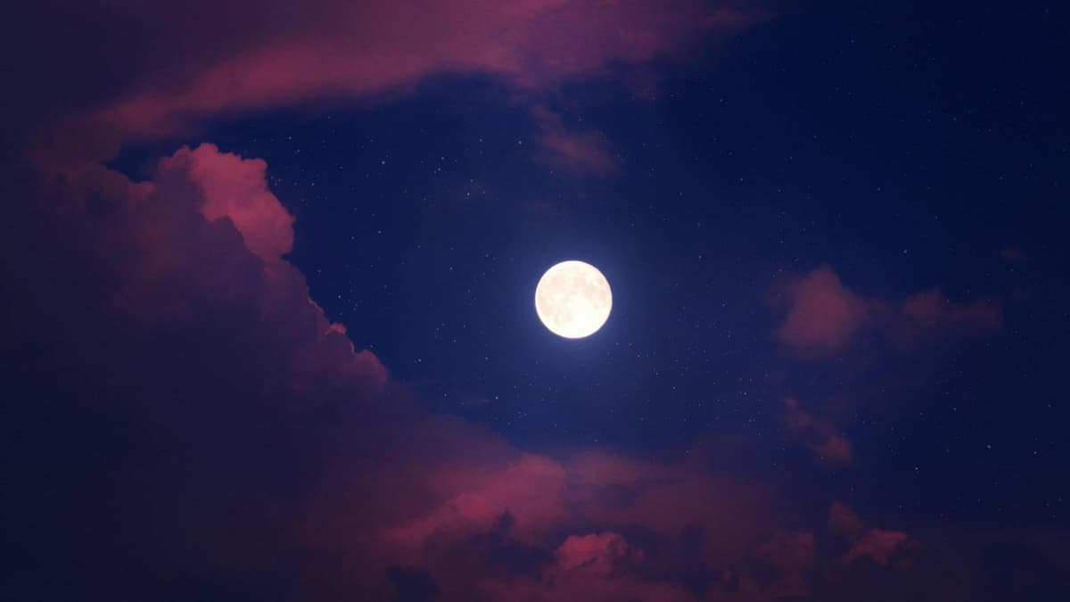 Ein Vollmond an einem blauen Himmel mit rosafarbenen Wolken.