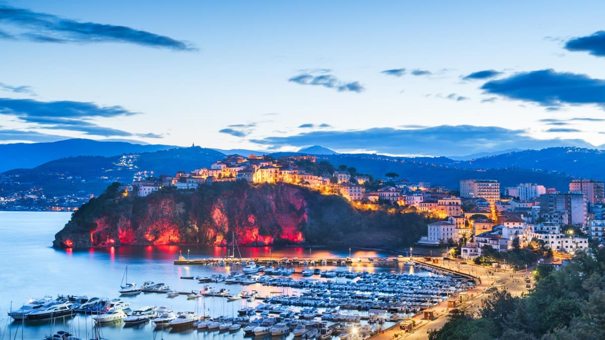 Cilento in der Dämmerung mit beleuchteten Häusern und dem Hafen mit Schiffen und Yachten.