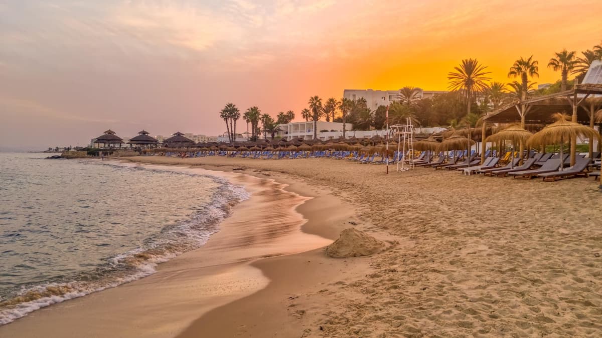 Ein Strand bei Sonnenuntergang in Tunesien mit Liegen und Schirmen.
