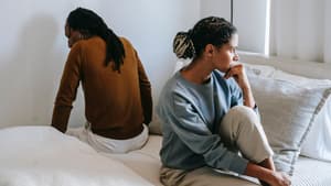 Mann und Frau sitzen mit dem Rücken zueinander auf einem Bett