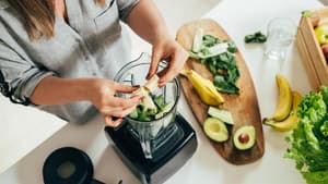 Frau legt Zutaten in einen Mixer