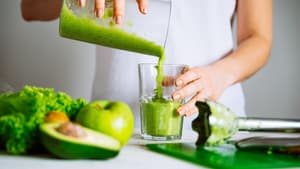 Frau im weißen T-Shirt bereitet einen grünen Smoothie vor