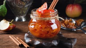 Bratapfelmarmelade im Glas steht auf einem Holztisch mit Zimtstangen