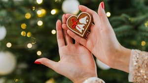 Frau hält ein Lebkuchenherz vor einem geschmückten Tannenbaum