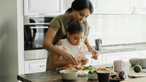 Frau mit Tochter bereitet Essen zu.