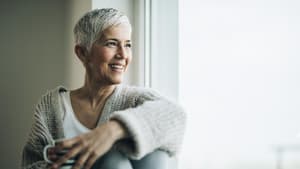 Frau mit kurzen grauen Haaren guckt aus dem Fenster.