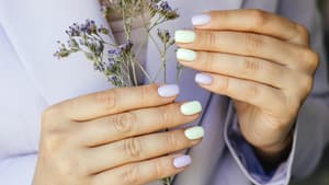 Hände mit bunten Fingernägeln und Blumen in der Hand.