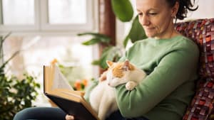 Frau mit Katze auf dem Schoß am Lesen.