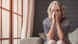 Frau sitzt auf dem Sofa und hält die Hände ins Gesicht.