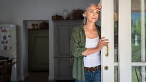 Frau lehnt im Türrahmen und schaut nach draußen.