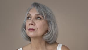 Frau mit grauen kurzen Haaren trägt eine weiße Bluse und Lippenstift.