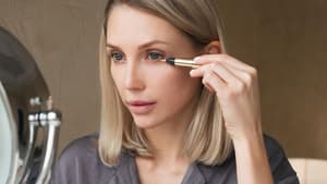 Frau sitzt vor dem Spiegel und trägt Concealer auf.