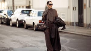 Frau trägt ein komplett braunes Outfit mit Hose, Pullover und Tasche und einer Sonnenbrille.