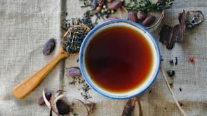 Eine Tasse Tee mit einem blauen Rand und verschiedenen Kräutern und Gewürzen drum herum.
