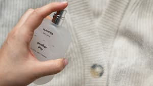 Jemand sprüht ein Parfum auf eine Strickjacke.