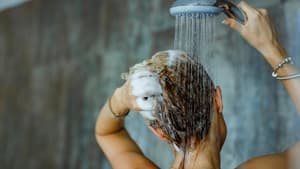 Frau wäscht sich in der Dusche die Haare und braust sie mit Wasser ab.