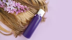 Haare einer Frau liegen mit Orchideen und einer lila Flasche auf einem rosafarbenen Hintergrund.