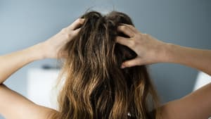 Frau von hinten fasst sich mit beiden Händen in die Haare an den Kopf.