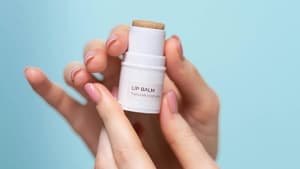 Ein Lip Balm wird in der Hand vor einem hellblauen Hintergrund gehalten.