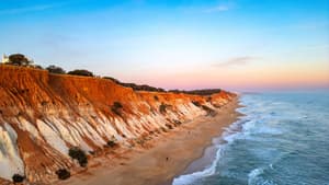 Rötliche Klippen und blaues Meer an der Praia da Falésia in Portugal.