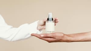 Eine Hand stellt ein Parfum in eine andere Hand.
