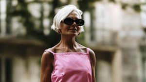 Ältere Frau mit grauen Haaren und Sonnenbrille trägt ein langes, pinkes Kleid.
