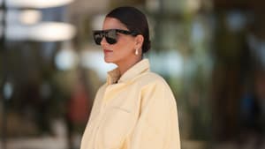 Frau mit einer gelben Jeansbluse, Sonnenbrille und einem niedrigen Dutt mit kurzen Haaren.