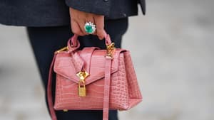 Eine kleine rosane Tasche wird von einer Hand mit einem Smaragd-Ring gehalten.