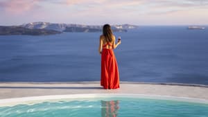 Frau steht in rotem Kleid am Pool und blickt aufs Meer.