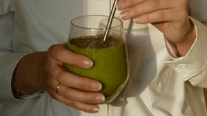 Frau hält ein Glas mit einem grünen Shake und einem Strohhalm in der Hand.