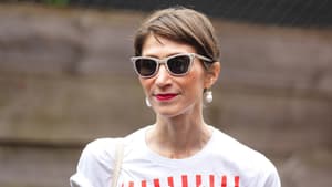 Frau mit braunhaarigem Kurzhaarschnitt, einer beigen Sonnenbrille und roten Lippen.