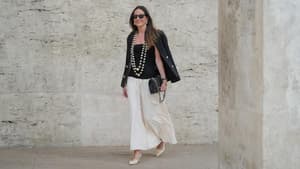 Frau trägt einen weißen Maxi-Rock im Boho-Stil mit einem schwarzen Top und Blazer und zwei großen Perlenketten.