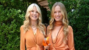 Christie und Sailor Brinkley in orangefarbenen langen Kleidern mit offenen lockigen Haaren und Sandalen.