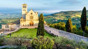Basilika von Assisi auf einem Hügel mit viel Grünfläche drum herum.
