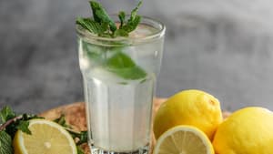 Ein großes Glas mit Wasser und frischer Minze drin, drum herum liegen aufgeschnittene Zitronen.