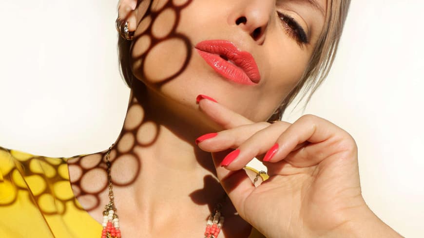 Frau mit korallfarbenem Lippenstift und Naegeln