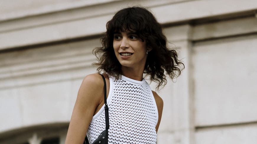 Frau auf Paris Fashion Week trägt weißes Kleid und lockige Haare mit Pony