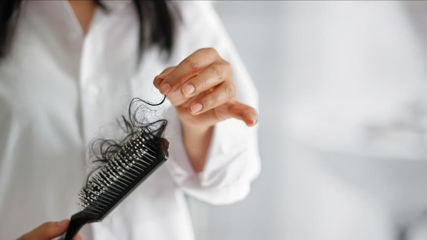 Frau hält Bürste mit Haaren in der Hand