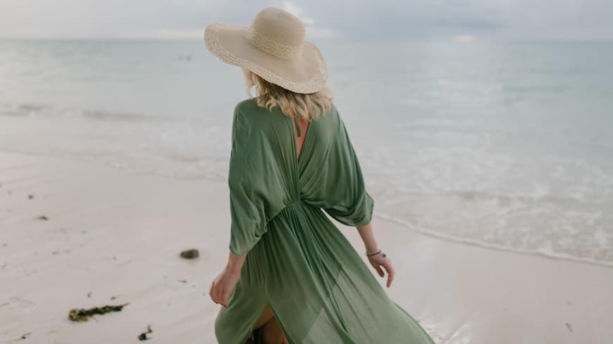 Frau mit grünem Kleid und Strohhut am Strand