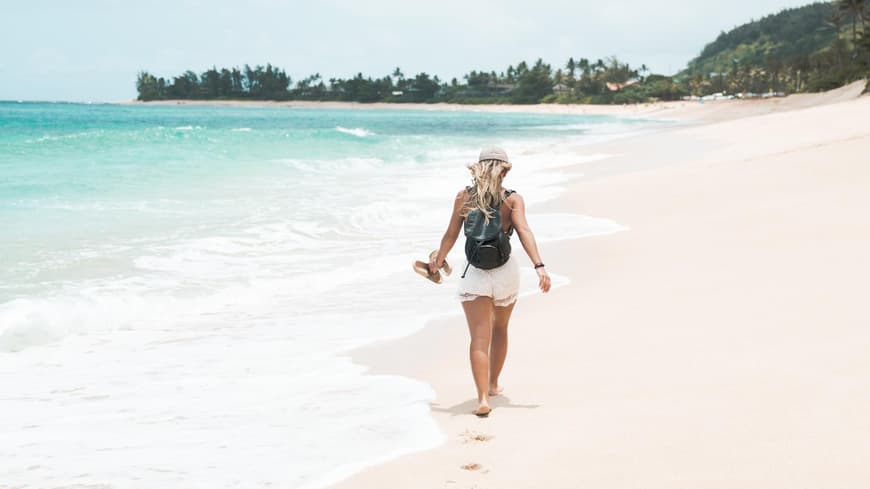 Frau mit weißen Shorts und Hut läuft am Strand
