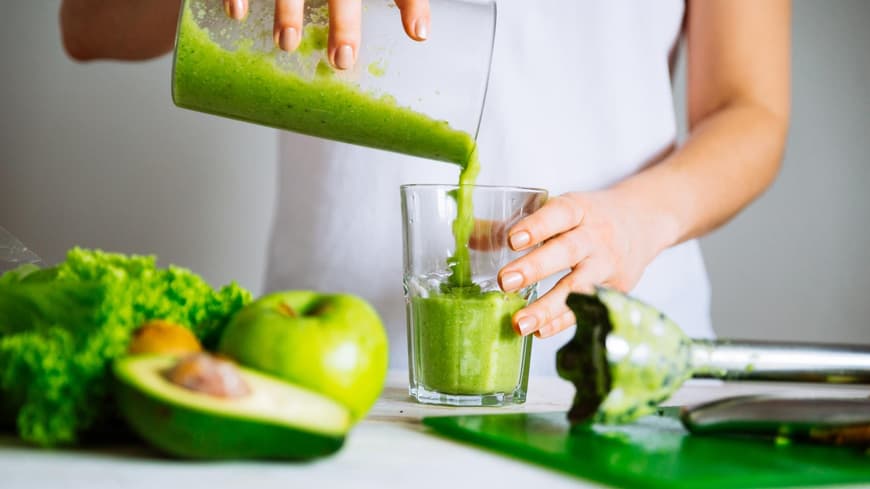 Frau im weißen T-Shirt bereitet einen grünen Smoothie vor