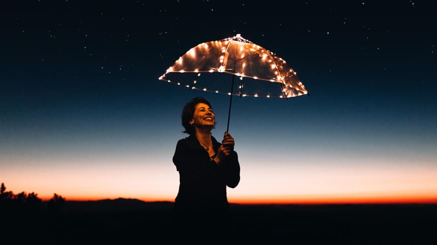 Frau mit bedeluchtetem Regenschirm schaut sich den Nachthimmel an