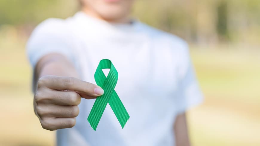 Frau im weißen T-Shirt hält eine grüne Schleife in die Kamera