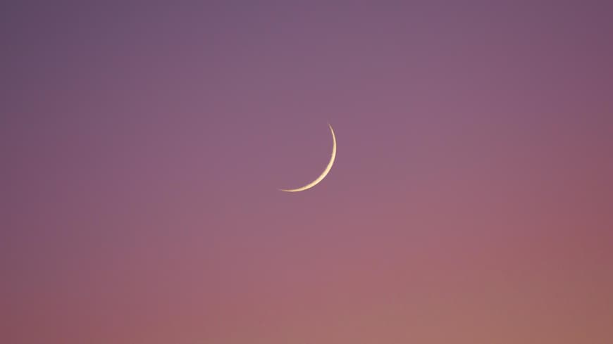 Neumond am rosa-orangefarbenen Himmel