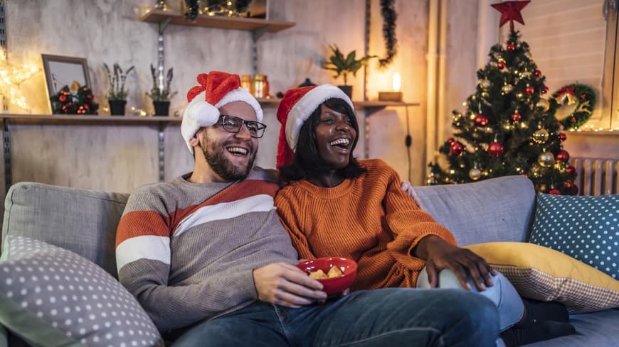 Glückliches Paar sitzt auf der Couch und guckt einen Weihnachtsfilm