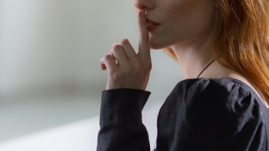 Frau hält ihren Zeigefinger vor ihren Lippen