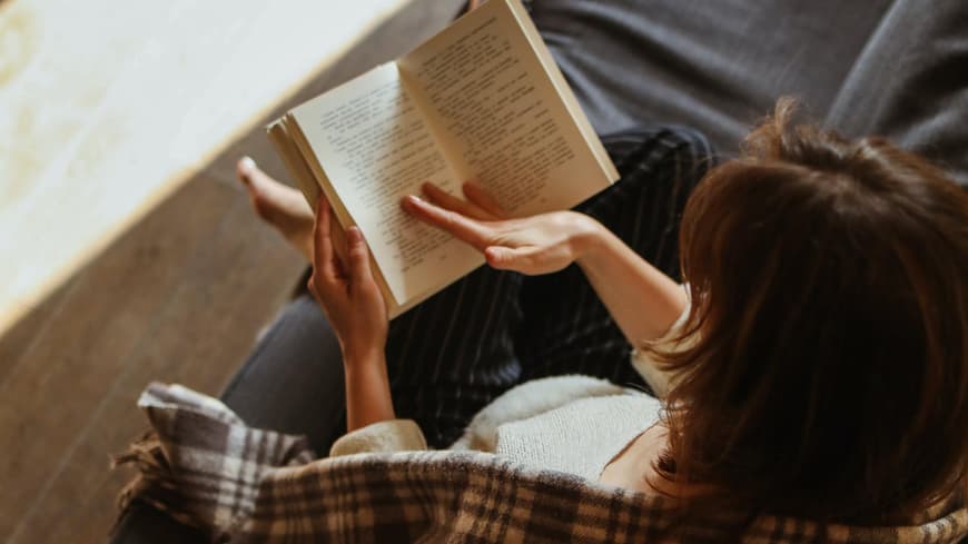 Frau sitzt mit einem Buch in der Hand auf der Couch